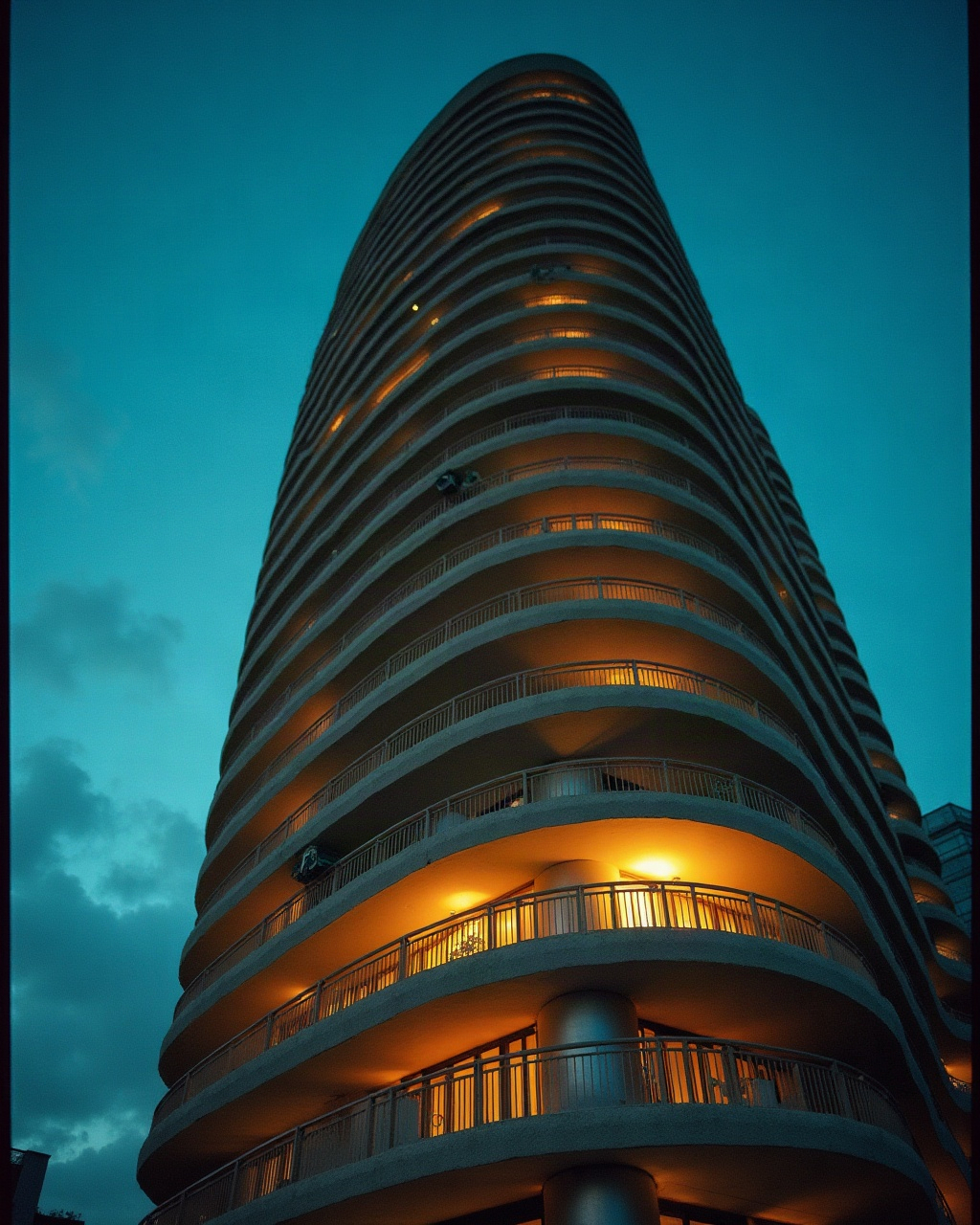 Ribbon balconies of a round waterfront hotel tower curving upward at dusk, roofline out of frame